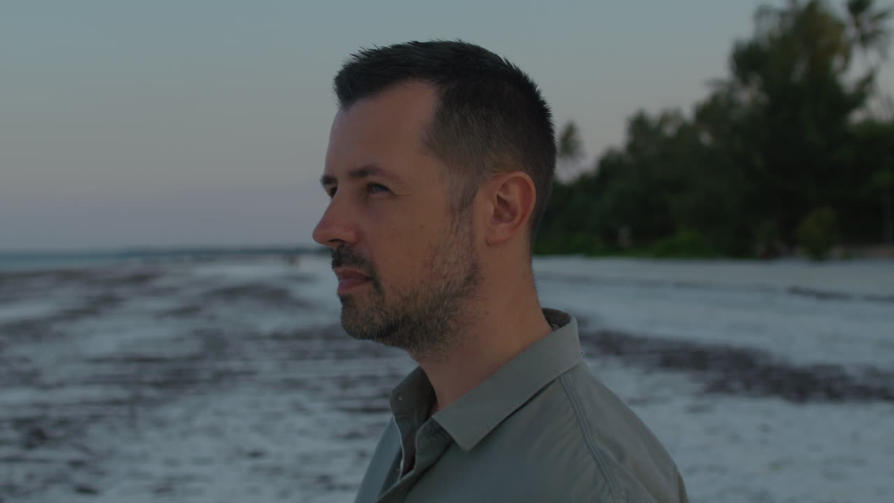 Close up on a thoughtful man walking alone towards ocean water on the remote tropical beach on the sunset.