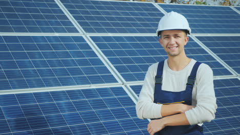 portrait of a young worker in a white helmet on the background of solar panels