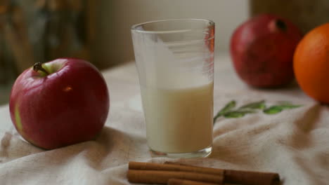 Glass-of-milk-with-red-apple-and-orange-on-tablecloth.-Breakfast-food