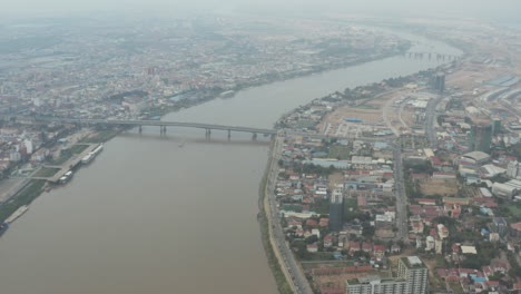 Langsamer-Luftschwenk-über-Phnom-Penh-Und-Tonle-Saugt-Seine-Brücke-An-Einem-Verschmutzten-Tag-Ab