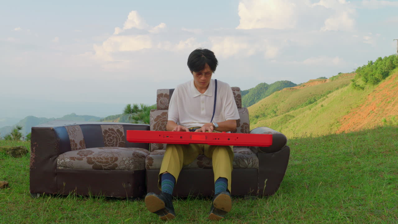 young artist musician playing a song with keyboard piano sitting in couch in outdoor valley mountains