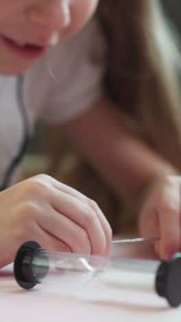 playful little girl connects sharp ends of metal pins at desk in classroom closeup. happy schoolgirl plays with stationery during craft lesson at school