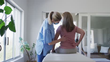 female health worker stretching back of senior woman at home