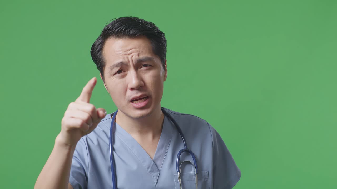 아시안 남성 의사가 스테토스코프를 들고 병원에서 녹색 화면 배경에 서서 카메라에 소리치고 있습니다.
