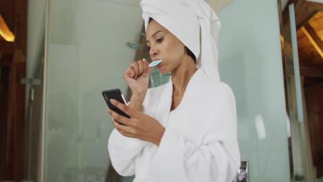 mujer de raza mixta cepillándose los dientes con un teléfono inteligente