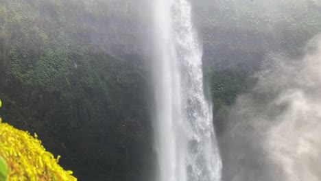 majestic nungnung waterfall cascading through lush jungle, surrounded by dense greenery and mist, slow establishing upward