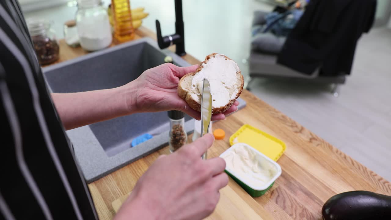 Spreading cream cheese on a slice of bread in the kitchen