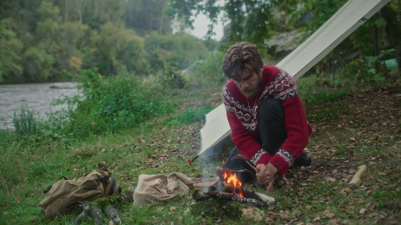 Man Cooking Food over Fire beside River and Tent during Solo Camping Trip