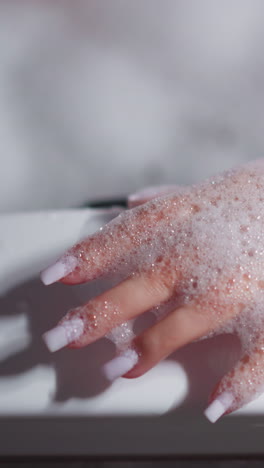 woman applies foam on manicured hand in bathtub closeup. elegant lady takes care of body with cosmetic products in bathtub at home. hygienic routine pleasure