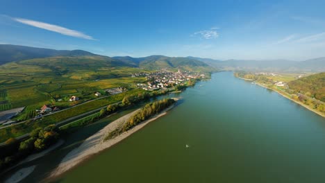 fpv ascending over the glistening river danube, smoothly approaching beautiful market town spitz, wachau, austria