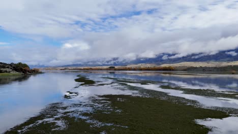 drone glides above tranquil wetlands with water reflections, lush greenery, and distant mountains under dramatic clouds. smooth forward camera movement, natural daylight