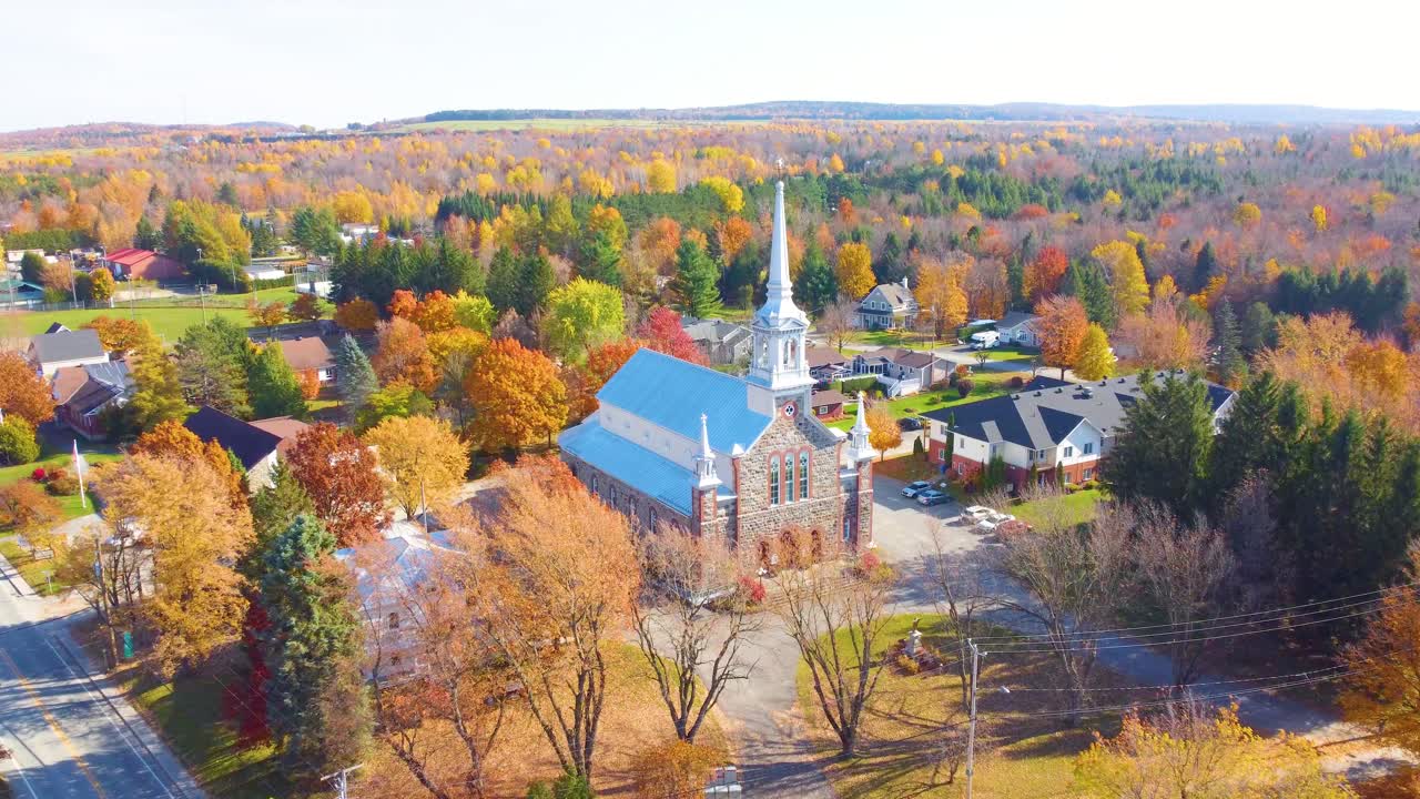 A small town in estrie, québec, with a church amid vibrant fall foliage, aerial view