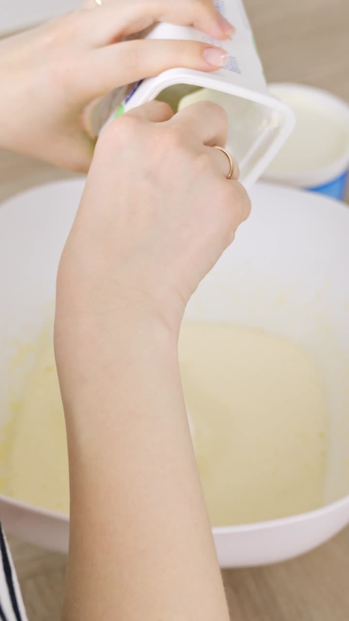 Hands using sppon to put whipped cream adding into tiramisu mixture inside bowl for the next recipe step, vertical