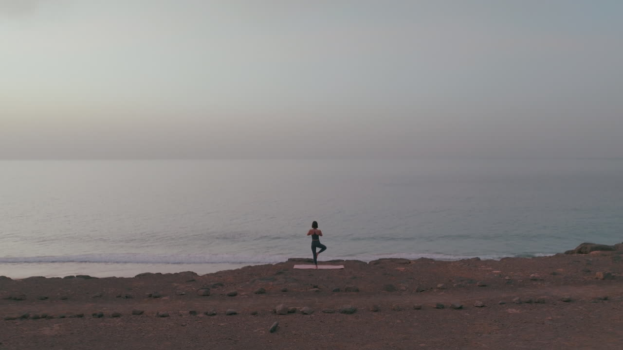 Woman practicing yoga on a beach cliff overlooking the ocean