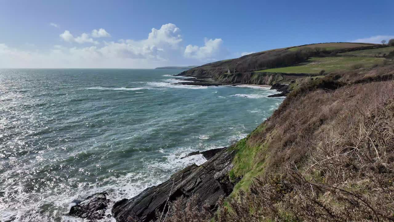 Rugged coast of Ireland on a sunny day in May with waves and green fields, wide panorama
