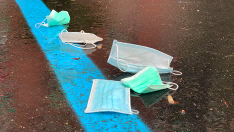 Pile-of-protective-facial-medical-masks-thrown-on-the-wet-ground-of-a-parking-lot-in-the-city