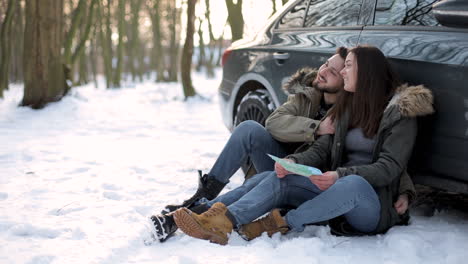 caucasian couple sitting in the snow and resting during a roadtrip.