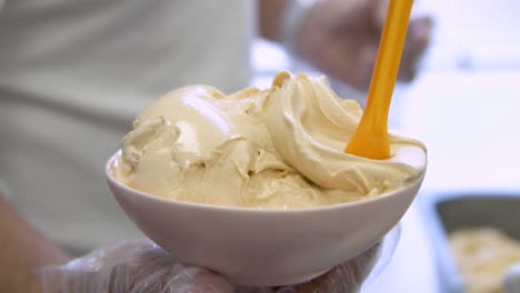 Bowl-of-salted-caramel-flavor-gelato-with-yellow-spoon-held-out,-closeup