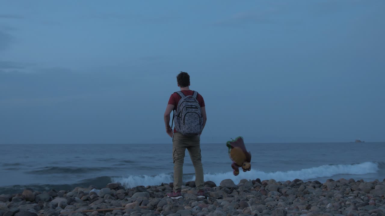 Giovane uomo in piedi da solo sulla spiaggia con un palloncino, pensieroso.