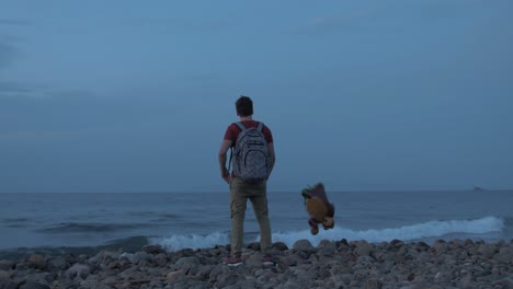 young man standing alone on beach with balloon contemplating