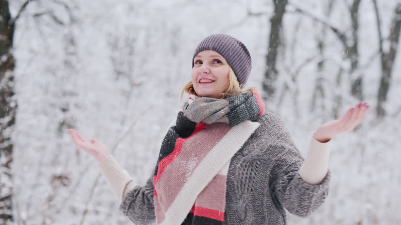 若い女性が冬の到来を喜ぶ冬の公園でスピンし、雪片をキャッチ