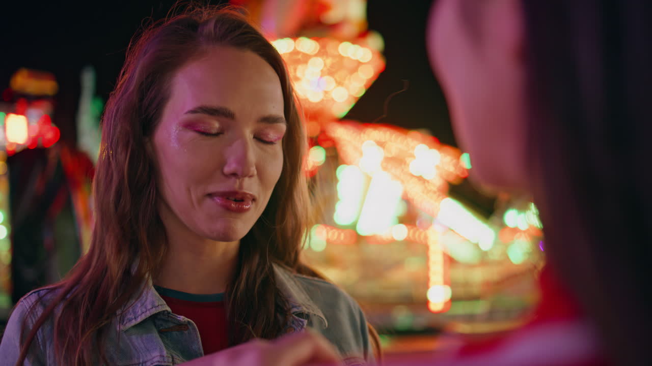 Closeup joyful girl talking friend at illuminated carousel. Happy smiling model