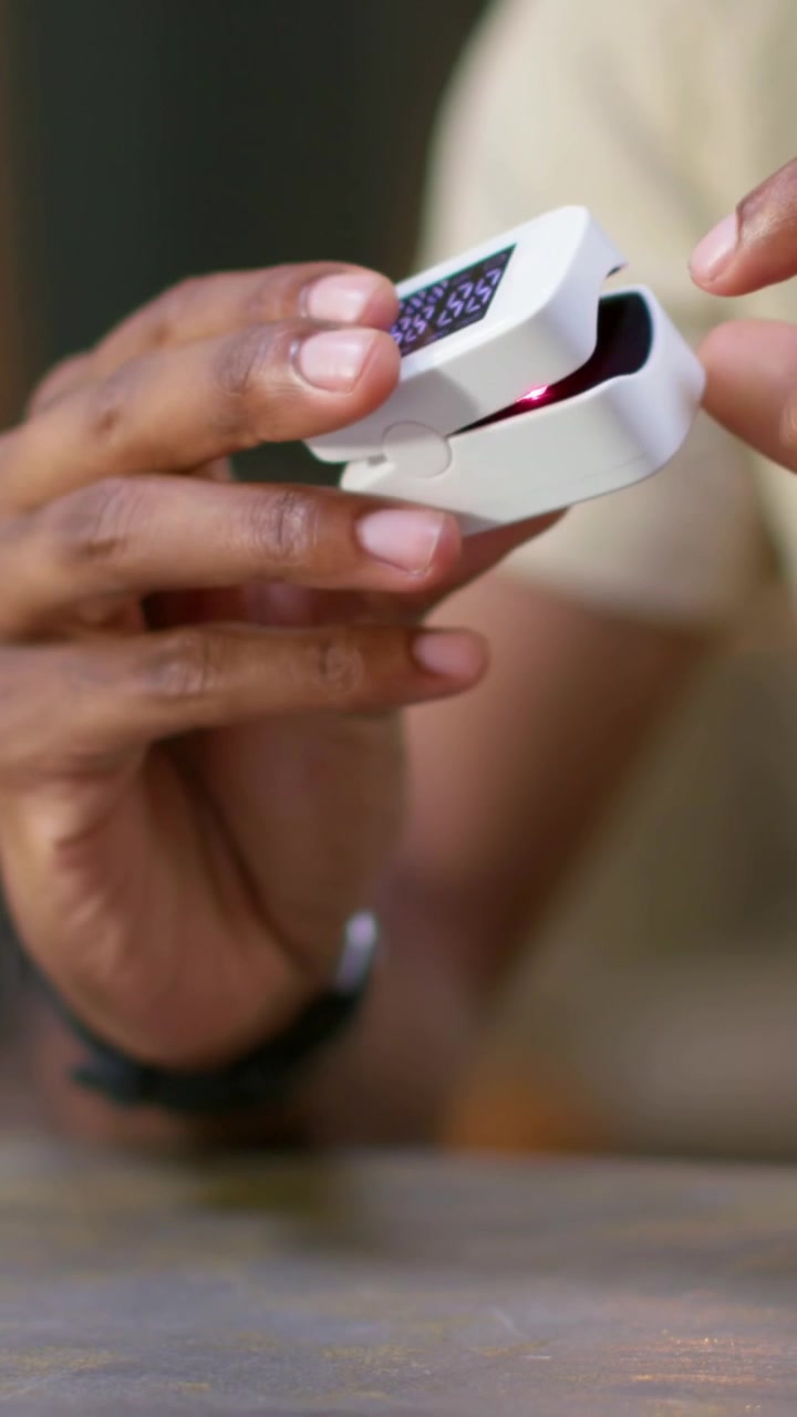 Vertical video: Shifting male hands picking fingertip into oximeter on table to check pulse, watch