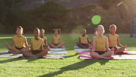 diverse group of schoolchildren sitting on mats meditating during yoga lesson outdoors