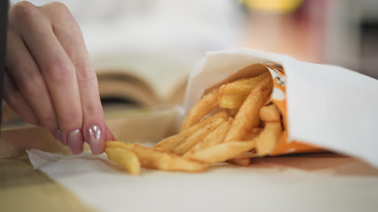 primer plano de la mano alcanzando patatas fritas crujientes de la bolsa de papel en la mesa en un entorno de comedor casual, fondo suave borroso con luces fuera de foco crea un ambiente cálido
