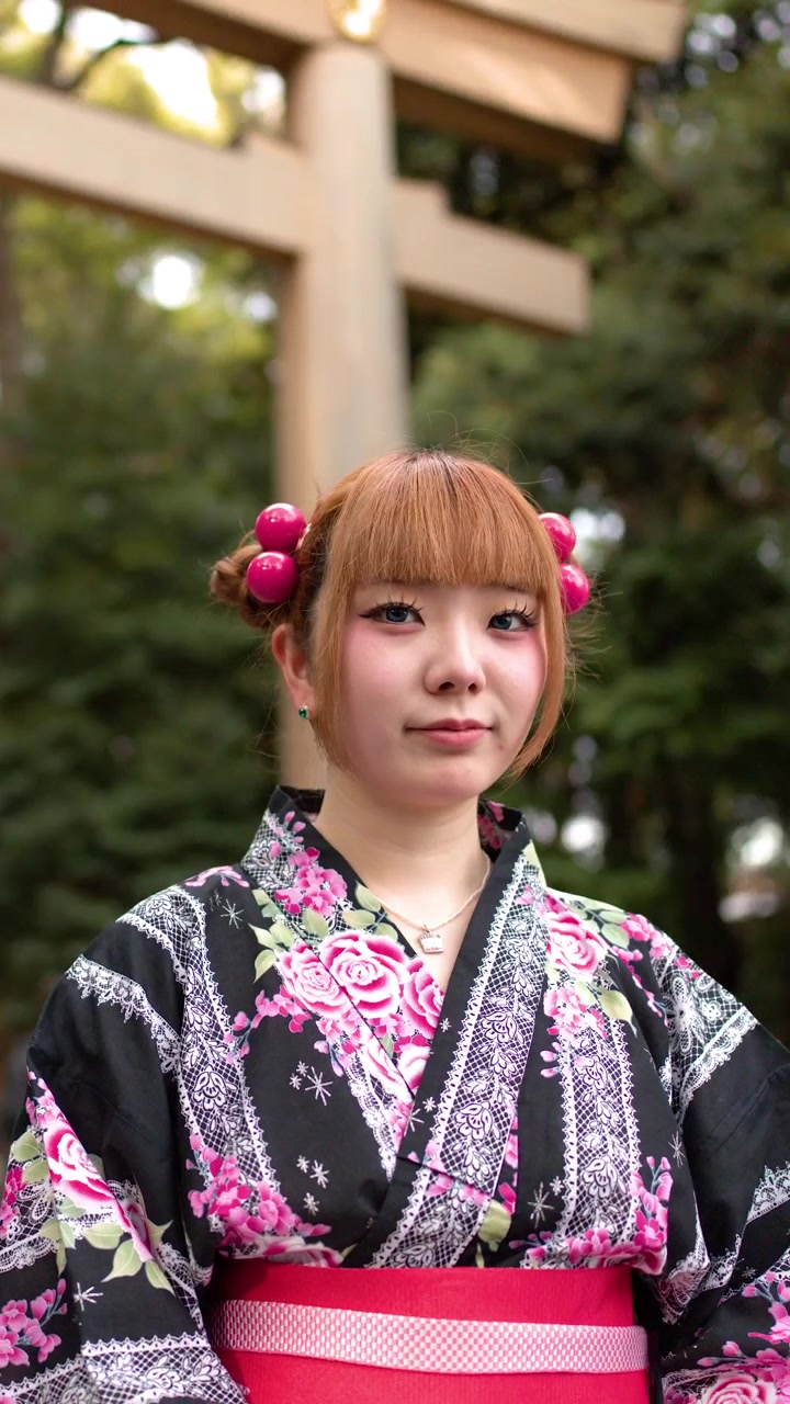 日中、花柄の浴衣を着た若い女性が日本の神社の外に立っています。