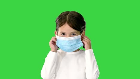 niña quitando la máscara de la cara y sonriendo a la cámara en una pantalla verde, clave de croma