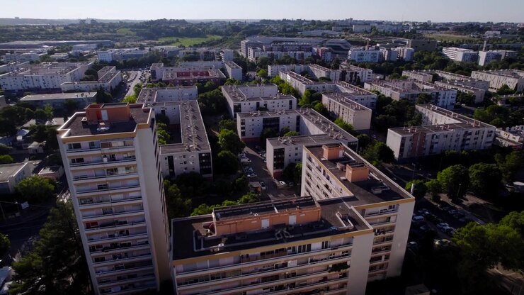 Vista aérea de drone de uma cidade com edifícios residenciais, árvores, parques de estacionamento e estradas de betão, luz solar ao final do dia
