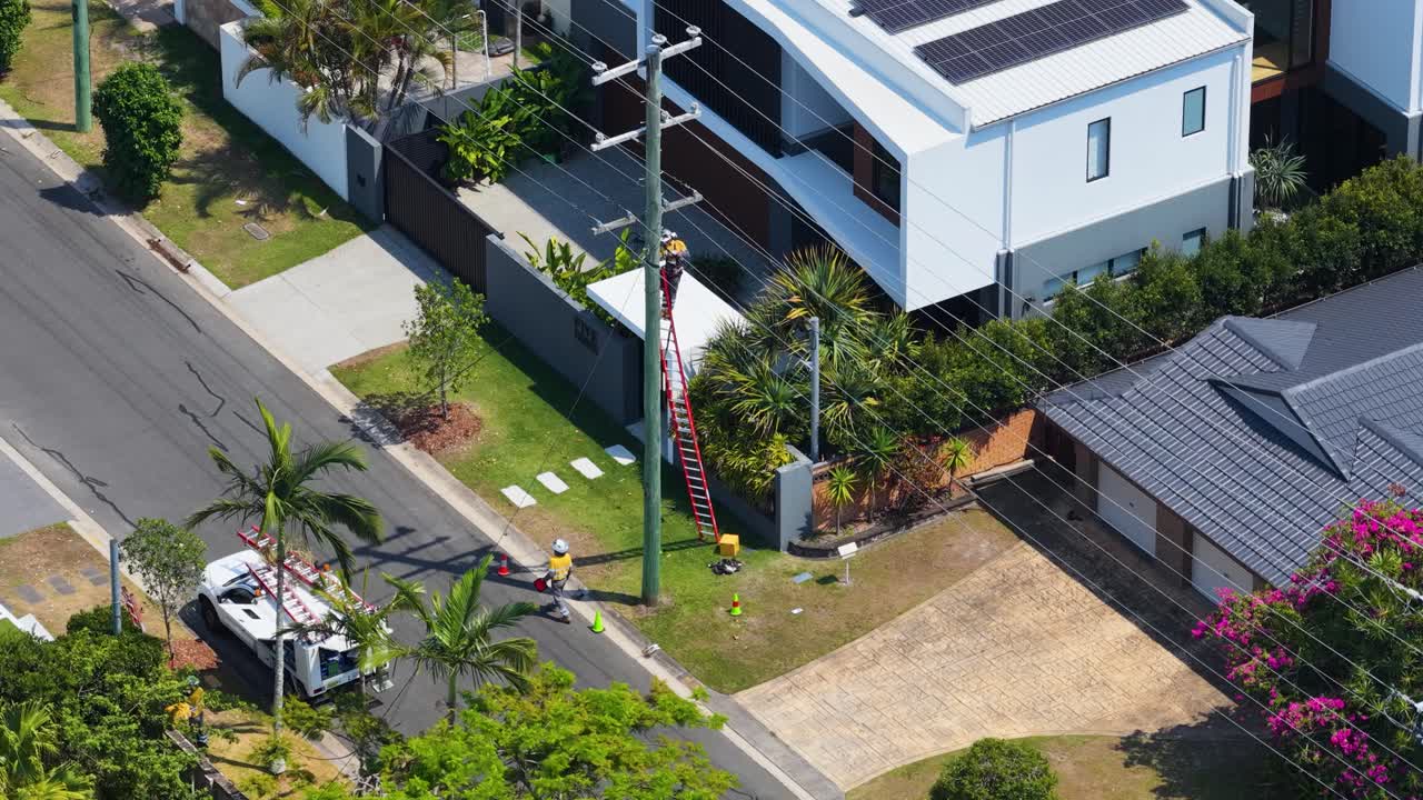 Aerial drone shot of utility worker inspecting residential power pole on sunny suburban street