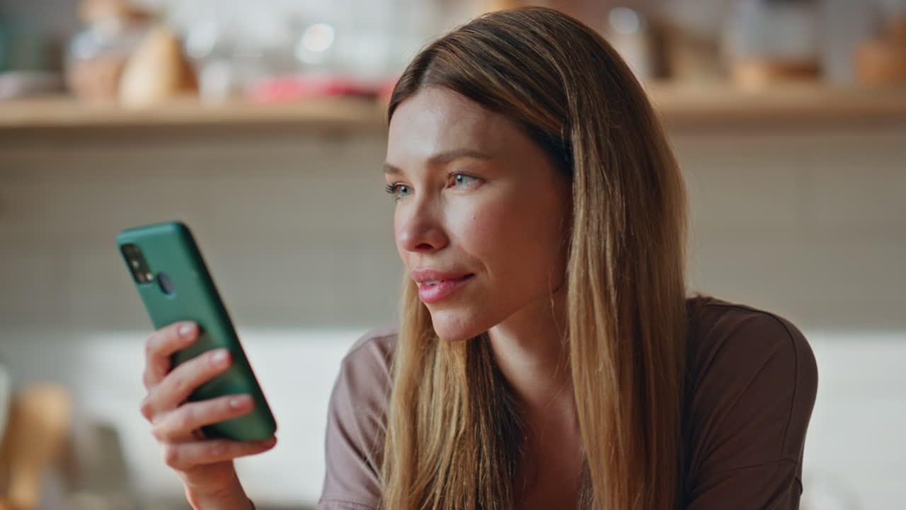 Porträt einer Frau, die in der Küche auf ihr Handy schaut. Attraktive Dame surft im Internet.