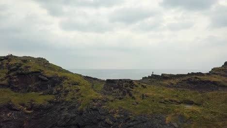 hiker standing on top of coastal cliffs in cornwall, uk, aerial flyover reveal