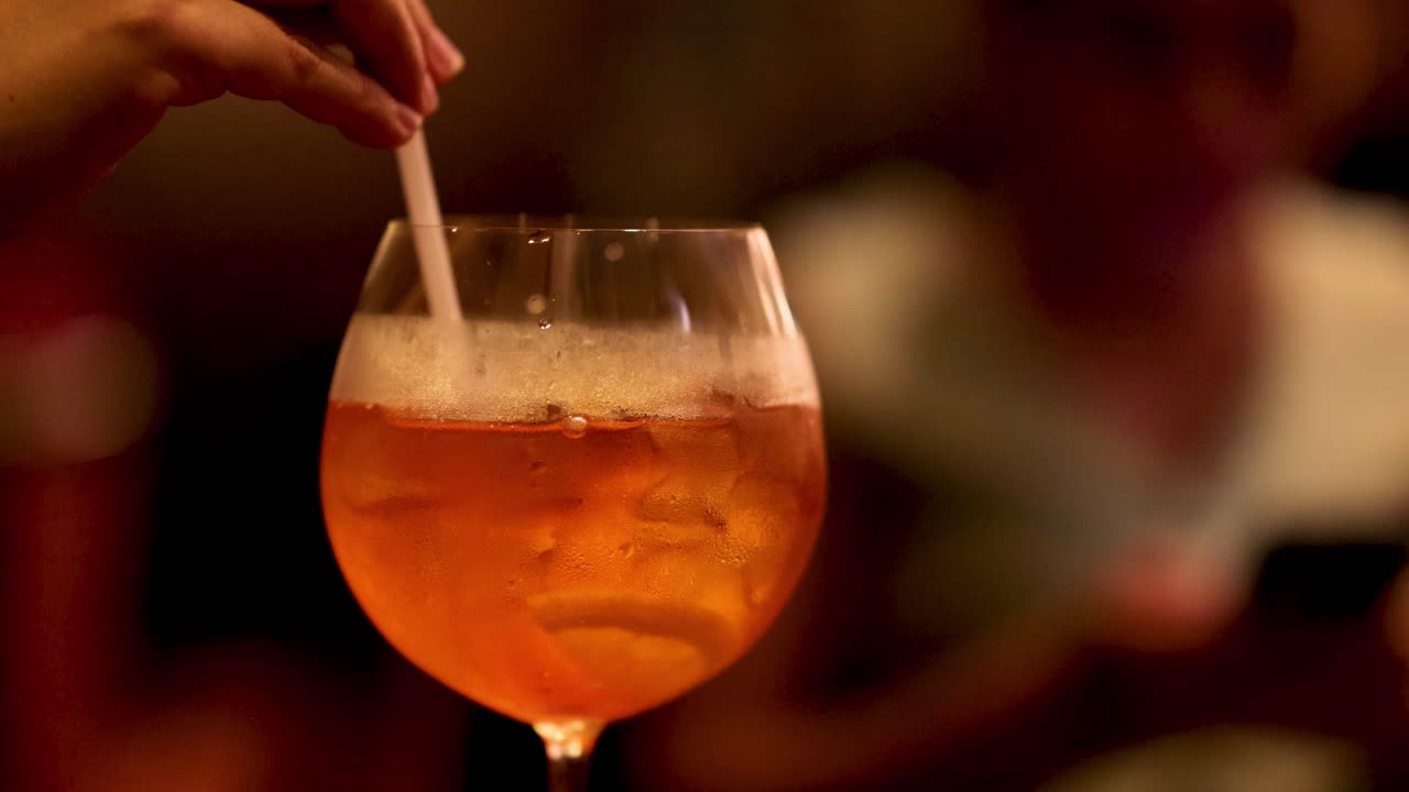Mano che mescola un cocktail con una cannuccia nel bicchiere