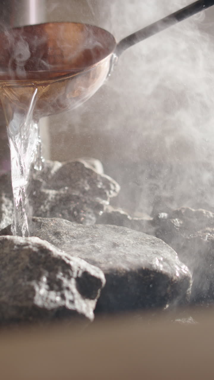 Steam rise from heated rocks as copper sauna ladle pours water on, vertical