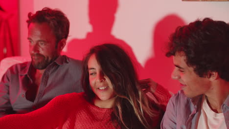 Cheerful-woman-sitting-on-sofa-with-men-and-switching-channels