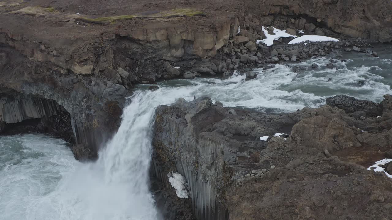 un hombre de pie en el borde de la roca del acantilado con una poderosa cascada que fluye en islandia