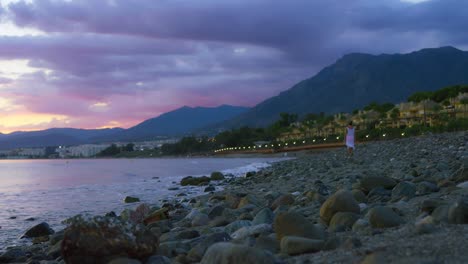 playa rocosa después de la puesta del sol con una mujer alejándose