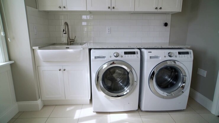 Sliding camera revealing front-load washer and dryer in home laundry room as window light shifting