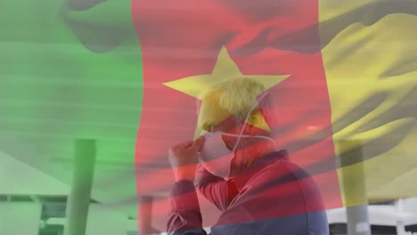 Animation-of-flag-of-cameroon-waving-over-caucasian-man-wearing-face-mask-in-city-street