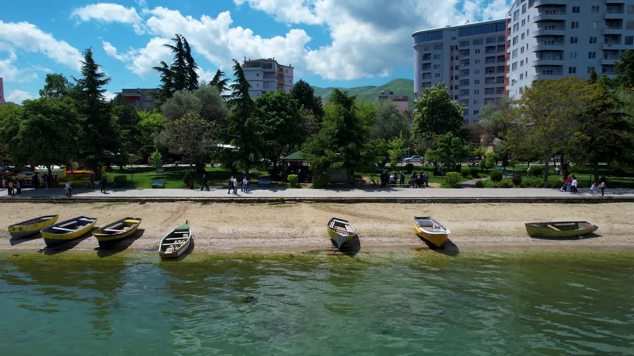 Ohrid Lake Park: A Serene Haven with Trees by Pogradec's Shoreline, Near Anchored Boats, Ideal for Tranquil Walks by the Clear Water