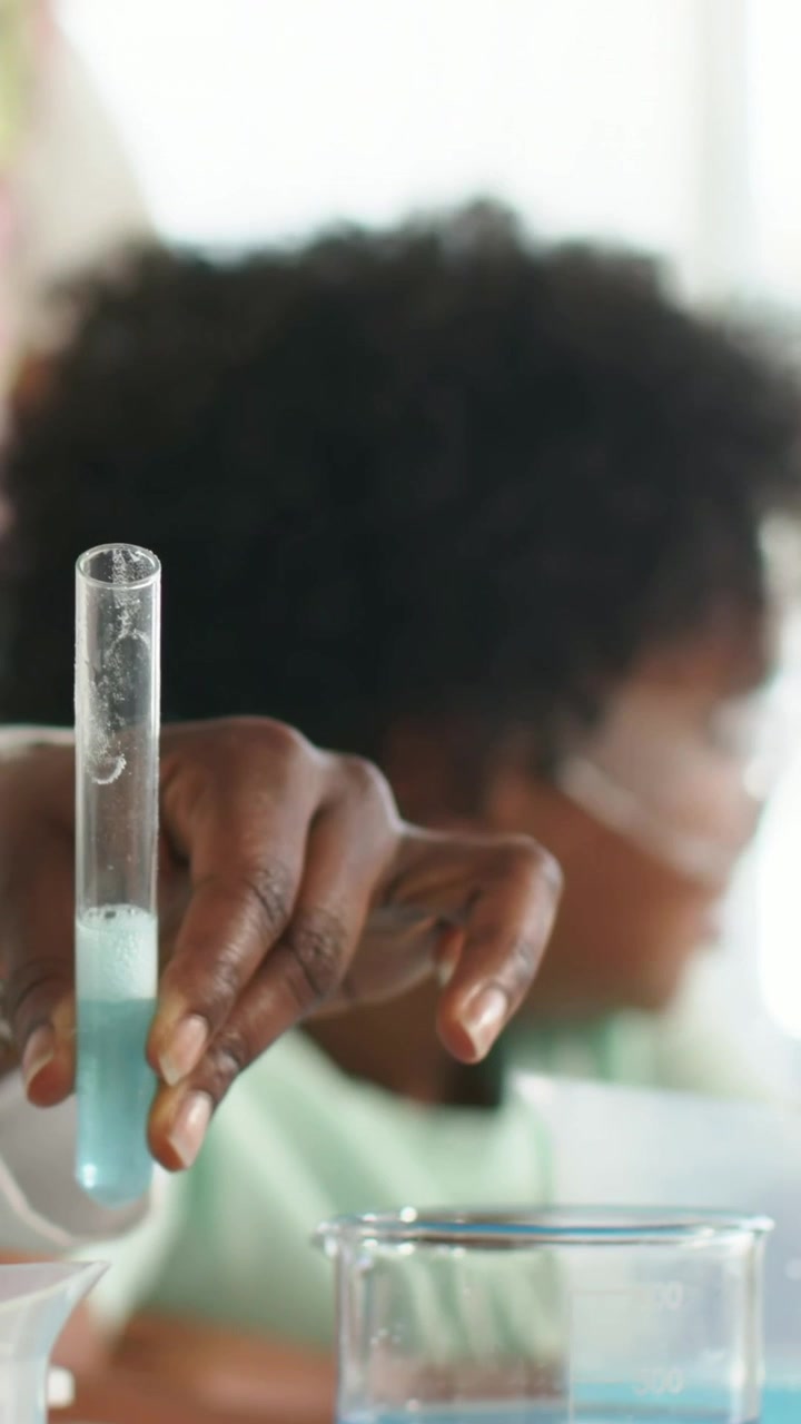 Vertical video: Holding test tube, adult in lab coat guiding youth donning goggles, copy space