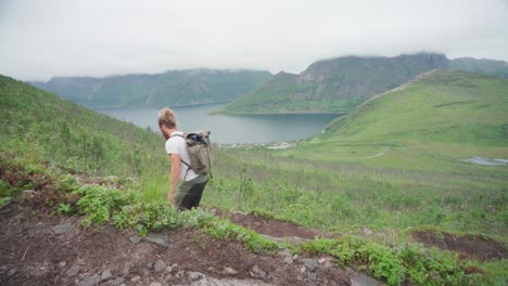 un excursionista masculino con una mochila subiendo cuesta arriba en el pintoresco lago de montaña en segla, isla senja, noruega