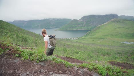 a male hiker with a backpack climbing uphill in scenic mountain lake at segla, senja island, norway