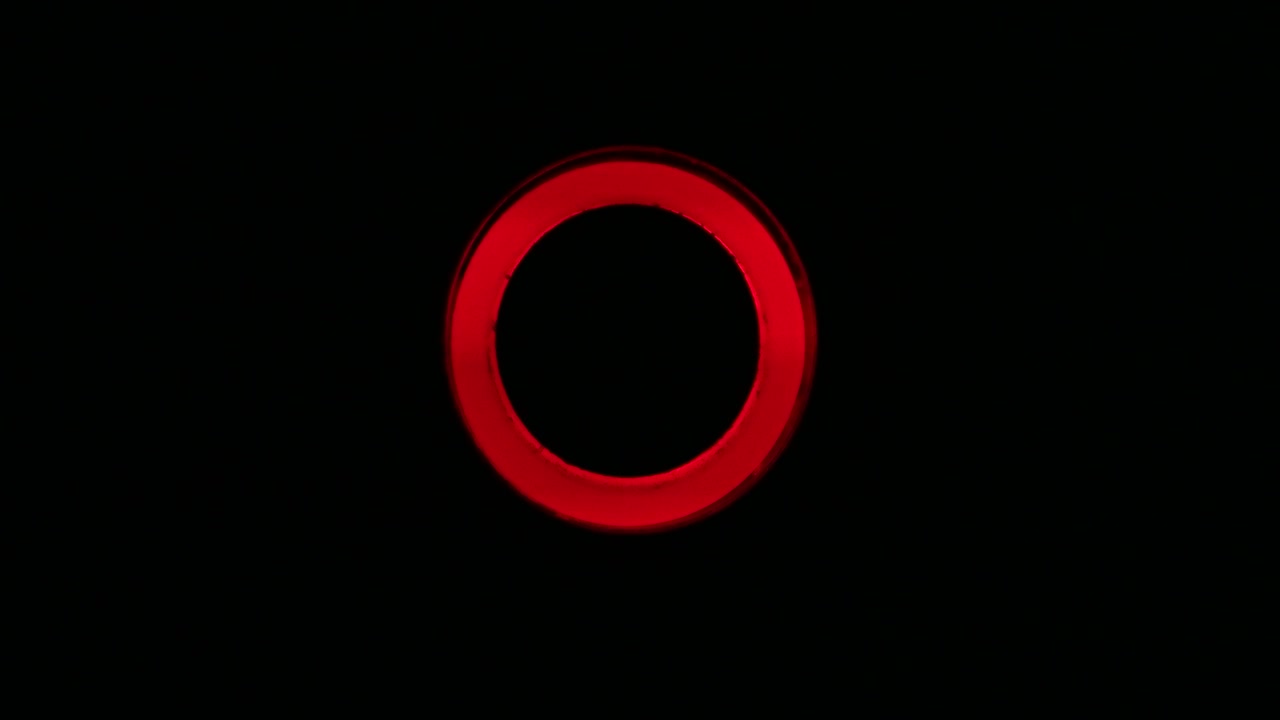 Pulsating red neon light of on-off switch. Macro close up, real time, no people, isolated on black, flickering