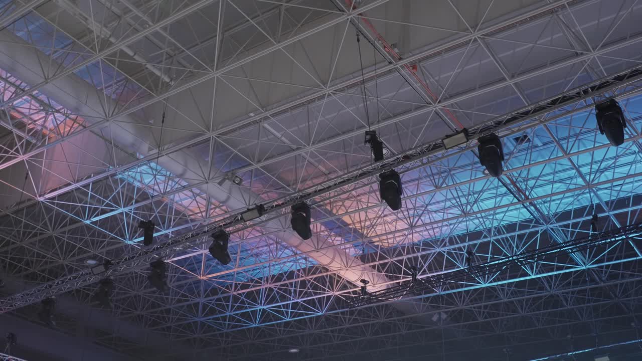 overhead view of metal roof trusses and suspended stage lighting inside large venue