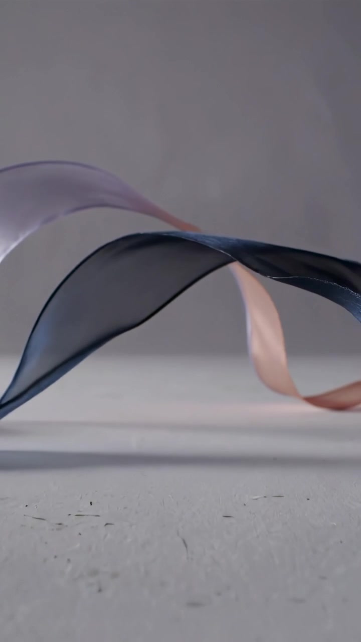 Video verticale: Nastri trasparenti che si sollevano mossi da una leggera brezza in studio, con bordi color crema e blu navy.