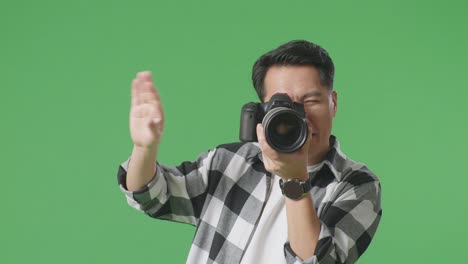 close up of asian photographer telling the model to move left and right while taking pictures by camera on green screen background in the studio